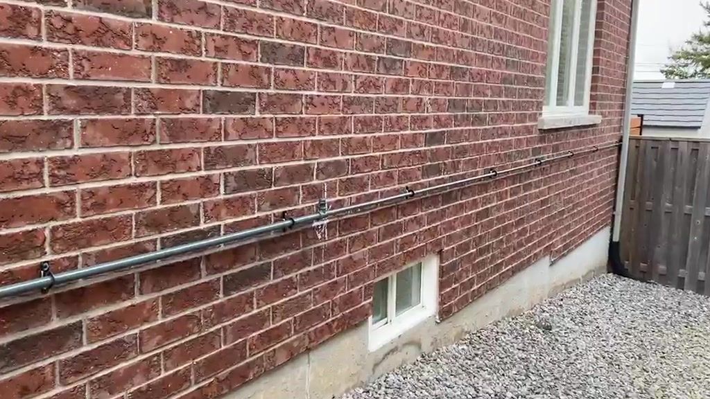 A gas line run along exterior brick, strapped at intervals